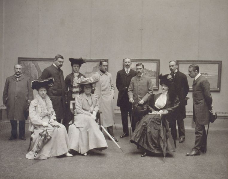 Schwarz-weiß Fotografie einer Gruppe von elf Personen, die die Ausstellung besuchen. 