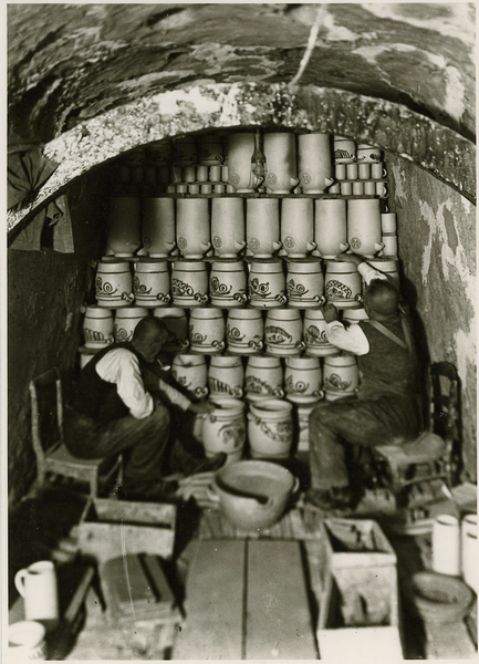 Historische schwarz-weiß-Fotografie, Zwei Männer sitzen in einem großen Ofen und setzen Keramikvasen.